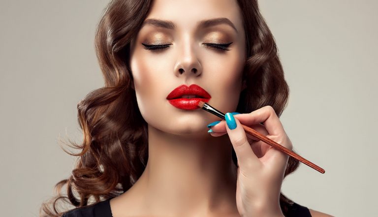 Makeup artist applies red lipstick . Beautiful woman face. Hand of make-up master, painting lips of young beauty model girl . Make up in process